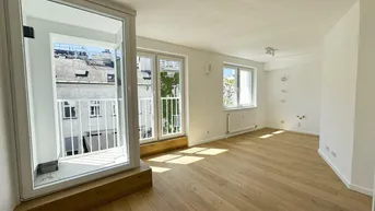Helles Zimmer mit Holzboden, weißen Wänden und Zugang zu einem kleinen Balkon.