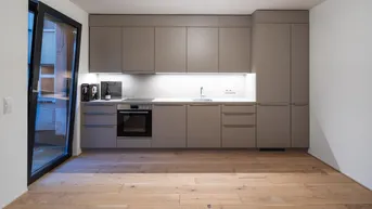 Moderne Küche mit beigefarbenen Schränken, Holzboden und Zugang zu einem Außenbereich.