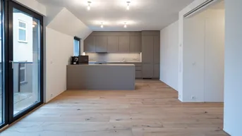 Heller offener Wohnbereich mit moderner Küche, Holzboden und Zugang zum Balkon.