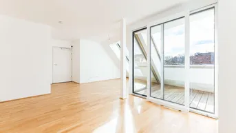 Helles Zimmer mit Holzboden, Dachschrägen und Zugang zu einem kleinen Balkon.
