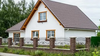 Weißes Einfamilienhaus mit braunem Ziegeldach, Holzfenstern und einem dekorativen Zaun.