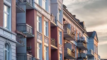 Historische Fassade eines Mehrfamilienhauses mit zahlreichen Balkonen unter einem bewölkten Himmel.
