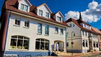 Gepflegtes Mehrfamilienhaus mit Mansarddach und großen Fenstern an einer städtischen Straße.