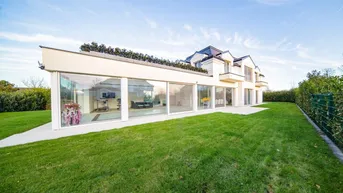 Moderne Villa mit großer Glasfassade und weitläufigem grünen Rasen unter blauem Himmel.