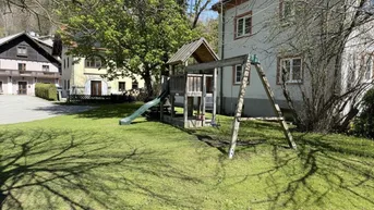 Großer Gartenbereich mit Kinderspielplatz und Schaukeln vor dem Gebäude.