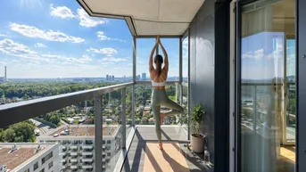 Sonniger Balkon mit weitem Stadtblick, Glasbrüstung und modernem Holzboden, ideal für Entspannung.