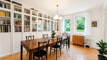 Helles Esszimmer mit großem Holztisch, Bücherregalen und Blick ins Grüne.