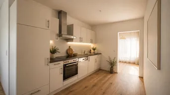 Moderne Einbauküche mit hellen Schränken, Holzboden und Zugang zu einem lichtdurchfluteten Raum.