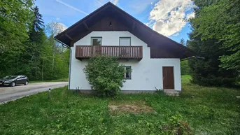 Charmantes Haus mit Holzbalkon und grüner Umgebung, umgeben von Bäumen und Natur.