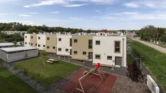 Moderne Reihenhäuser mit Flachdach, umgeben von Grünflächen und einem Kinderspielplatz.