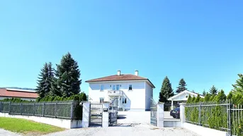 Großzügiges Anwesen mit repräsentativem Eingangstor und gepflegter Auffahrt unter blauem Himmel.