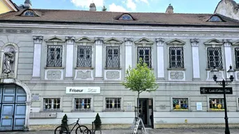 Historisches Gebäude mit klassischer Fassade, verzierten Fenstern und Geschäften im Erdgeschoss.