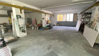 Geräumiger Werkstatt- oder Lagerbereich mit Betonboden und großen Fenstern, der Renovierungsbedarf zeigt.