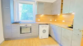Funktionale Küche mit grauen Schränken, Holzoptik-Arbeitsplatte und integriertem Backofen.