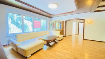 Geräumiges Wohnzimmer mit hellem Parkettboden, großen Fenstern und traditioneller Holzdecke.