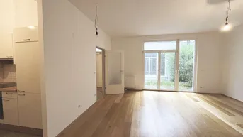Helles Wohnzimmer mit Holzparkettboden und Zugang zu einem kleinen Gartenbereich.