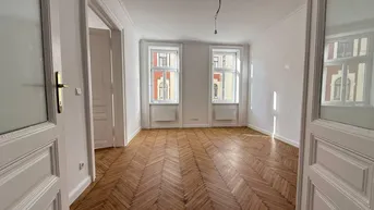 Helles Zimmer mit Fischgrätparkettboden und zwei großen Fenstern, bereit zur individuellen Gestaltung.