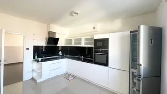 Moderne Einbauküche mit weißen Schränken, dunkler Arbeitsplatte und integrierten Geräten.