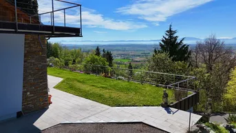 Geräumige Terrasse mit Steinplatten und weitem Blick über die grüne Landschaft und Berge.