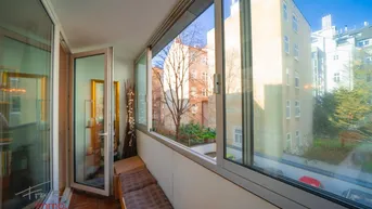 Verglaste Loggia mit Sitzbank und Blick auf den Innenhof und umliegende Gebäude.