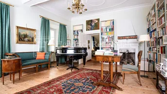 Geräumiges Wohnzimmer mit Flügel, Bücherregalen, Kamin und Holzdielenboden.