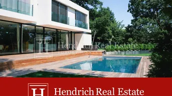 Moderne Villa mit großem Pool und Holzterrasse, umgeben von üppigem Grün und Bäumen.