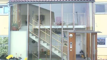 Eingangsbereich eines Mehrfamilienhauses mit verglastem Treppenhaus und Balkonen.