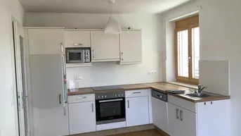 Funktionale Einbauküche mit weißen Schränken, Holz-Arbeitsplatte und integrierten Geräten.