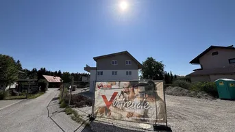 Neubau im Bau mit Werbebanner auf sonnigem Grundstück und blauer Himmel.