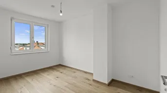 Helles Schlafzimmer mit Holzboden und Fenster, das einen weiten Blick über die Stadt ermöglicht.