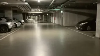 Geräumige Tiefgarage mit mehreren Stellplätzen und sichtbaren Versorgungsleitungen an der Decke.