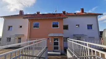 Moderne Wohngebäude mit hellen Fassaden und barrierefreien Zugangsrampen unter blauem Himmel.