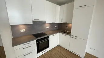 Moderne Einbauküche in Weiß mit dunkler Arbeitsplatte und Holzboden, bereit zur Nutzung.