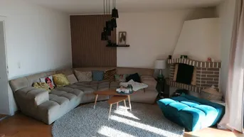 Gemütliches Wohnzimmer mit großem Ecksofa, Kamin und Holzboden, hell durchflutet.