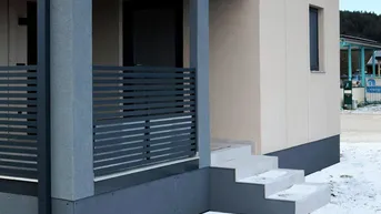 Moderne Gebäudefassade mit überdachtem Eingangsbereich und Treppe im Schnee.
