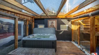 Überdachter Wellnessbereich mit Whirlpool, Sauna und Holzboden unter einem Glasdach.