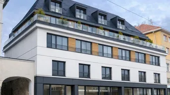 Modernes Gebäude mit weißer und dunkelgrauer Fassade, großen Fenstern und Mansarddach mit Dachterrasse.