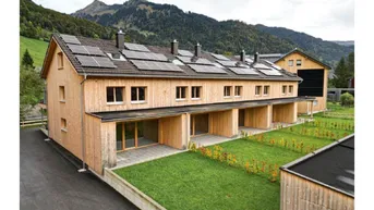 Moderne Reihenhäuser mit Holzfassade, Solaranlagen auf dem Dach und Blick auf die Berge.