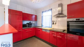 Moderne Küche mit roten Hochglanzfronten, integrierten Geräten und Fliesenboden.