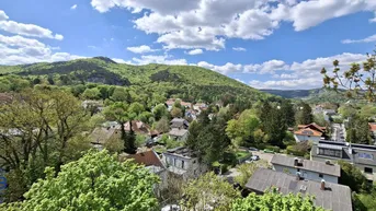 Panoramablick über eine grüne Hügellandschaft mit verstreuten Häusern unter blauem Himmel.