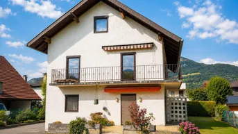 Weißes Einfamilienhaus mit braunem Satteldach, Balkonen und Bergblick in sonniger Lage.