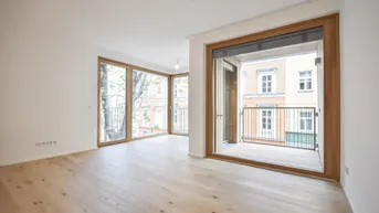 Helles Wohnzimmer mit Holzboden und Zugang zu einem kleinen Balkon, umgeben von Stadtbäumen.