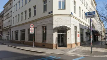 Außenansicht eines Eckgebäudes mit Ladenlokalen im Erdgeschoss und Straßenblick.