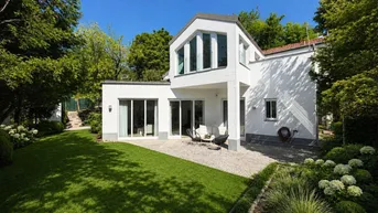 Moderne weiße Villa mit gepflegtem Garten, Rasenfläche und sonniger Terrasse.