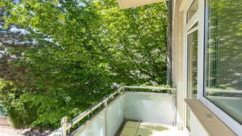 Heller Balkon mit Blick ins Grüne, umgeben von Bäumen und Pflanzen.