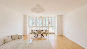 Helles Wohn- und Esszimmer mit Parkettboden, bequemer Couch und großzügigen Fenstern.