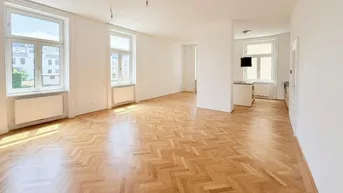 Helles, geräumiges Wohnzimmer mit Fischgrätparkett und großen Fenstern, die viel Tageslicht hereinlassen.