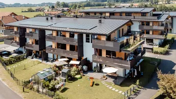 Luftaufnahme moderner Mehrfamilienhäuser mit Balkonen, Gärten, Solaranlagen und ländlicher Umgebung.
