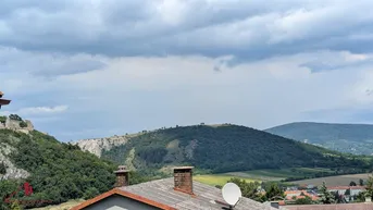 Weitläufiger Blick über hügelige Landschaft und Dächer, mit bewölktem Himmel.