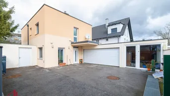 Moderne Hausfassade in Beige mit integrierter Garage und großem Vorplatz.